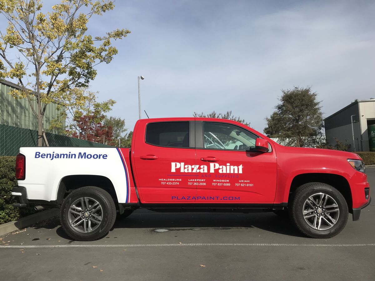 Red and white Chevrolet Colorado pickup carrying Plaza Paint graphics on the doors and a Benjamin Moore panel on the bed side
